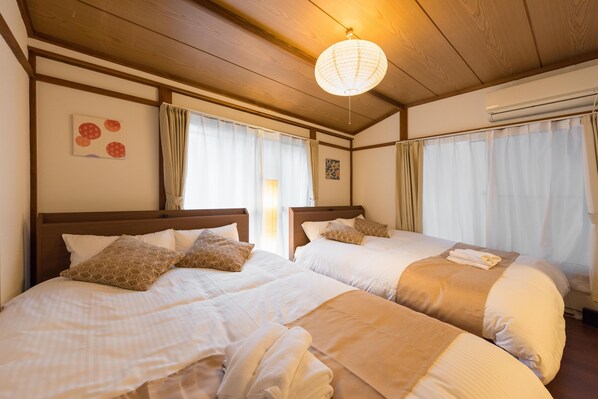 Habitación de hotel con dos camas, cabeceros de madera, una lámpara en el techo y aire acondicionado montado en la pared.