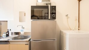 A compact kitchen with a stainless steel refrigerator, a microwave, and a built-in oven. - Yoshinaga Apartment 103 (Tokyo)