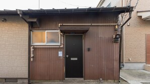 A brown metal gate with a window and a door, a small sign, and a utility box. - Yoshinaga Apartment 103 (Tokyo)