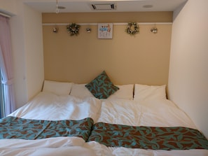 A neatly made bed with white and green patterned bedding, a single decorative pillow, and a wall-mounted sign above. - Lyon Doll Shinjuku Gyoen 401 (Tokyo)