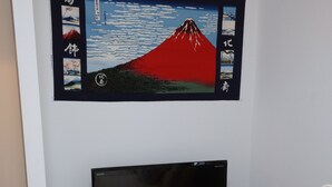 A living room with a mounted artwork of Mount Fuji, a flat-screen TV, a red suitcase, and a white sofa. - Lyon Doll Shinjuku Gyoen 401 (Tokyo)