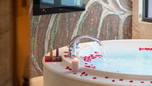 A bathtub with rose petals and a candle, a television mounted on the wall, and a window with a view of trees. - Royal Group Motel Jhong Hua Branch (Kaohsiung)