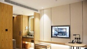 A modern hotel room with a bed, a small table, a TV, and a bathroom with a mirror and sink. - Wassim Hotel (Shanghai)