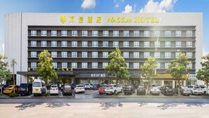 A hotel with multiple floors, a parking lot, and several trees in front. - Wassim Hotel (Shanghai)