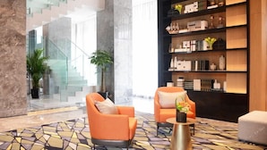 A modern lobby with orange armchairs, a patterned floor, a bookshelf with decorative items, and a staircase in the background. - Wassim Hotel (Shanghai)