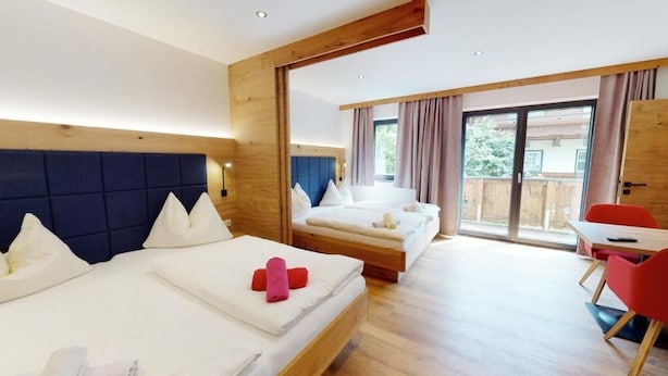 Een hotelkamer met twee bedden, een houten hoofdbord, een balkon met schuifdeur en een rode stoel.