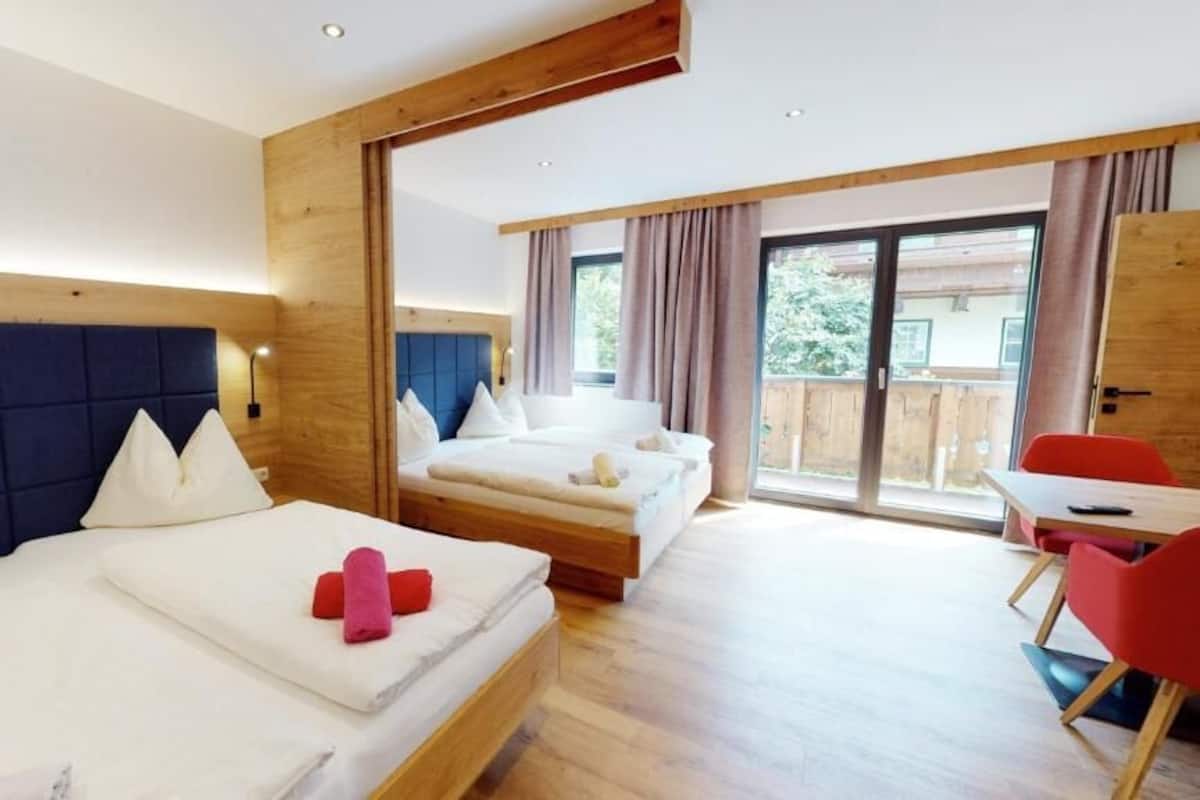 Une chambre d’hôtel avec deux lits, une tête de lit en bois, un balcon avec une porte coulissante et une chaise rouge.