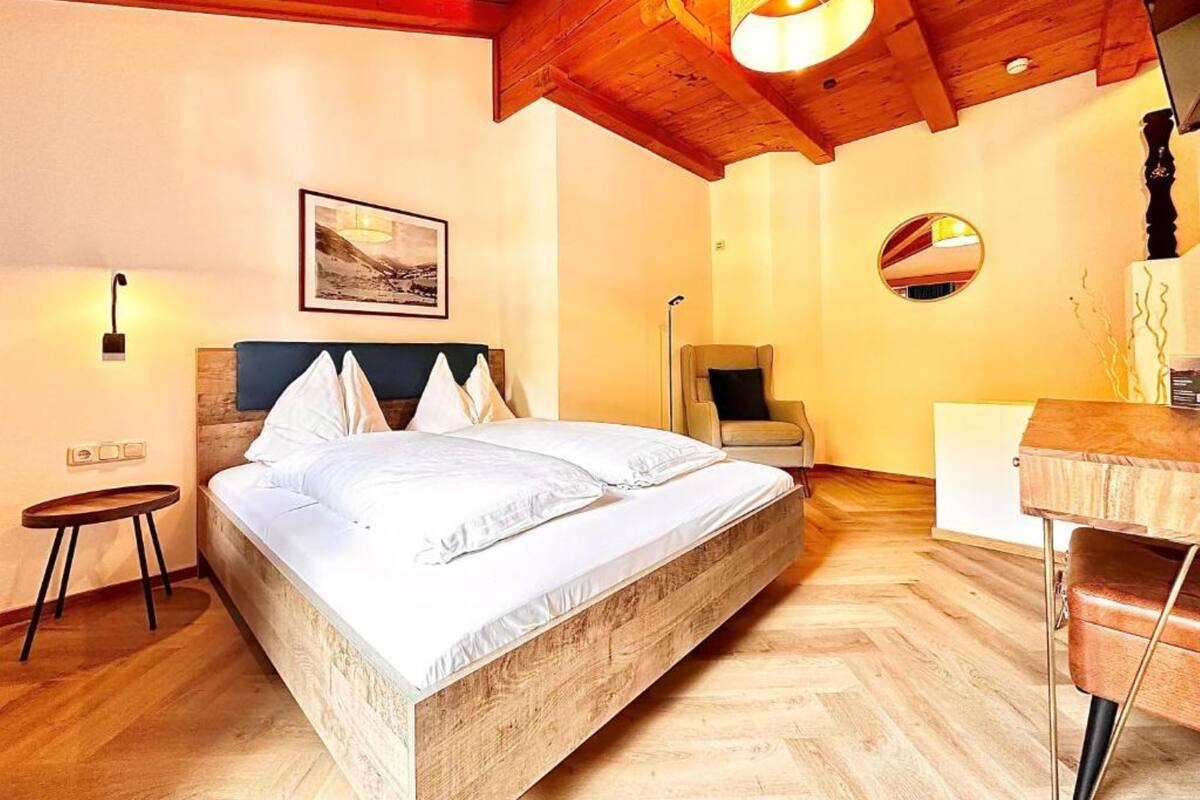 Une chambre avec un lit en bois, un bureau, une chaise et un luminaire suspendu.