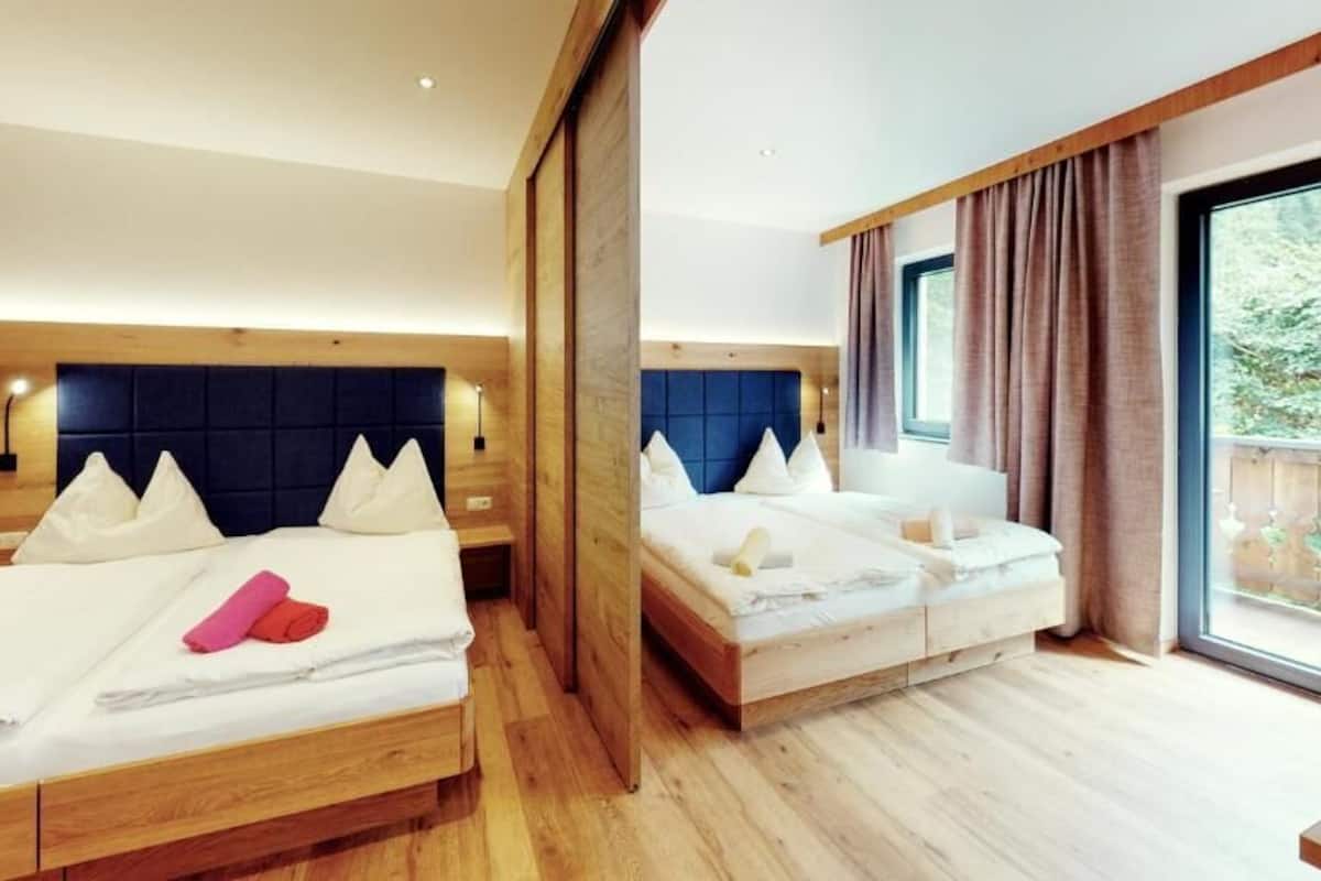 Une chambre d’hôtel avec deux lits, des têtes de lit en bois et une grande fenêtre avec des rideaux.