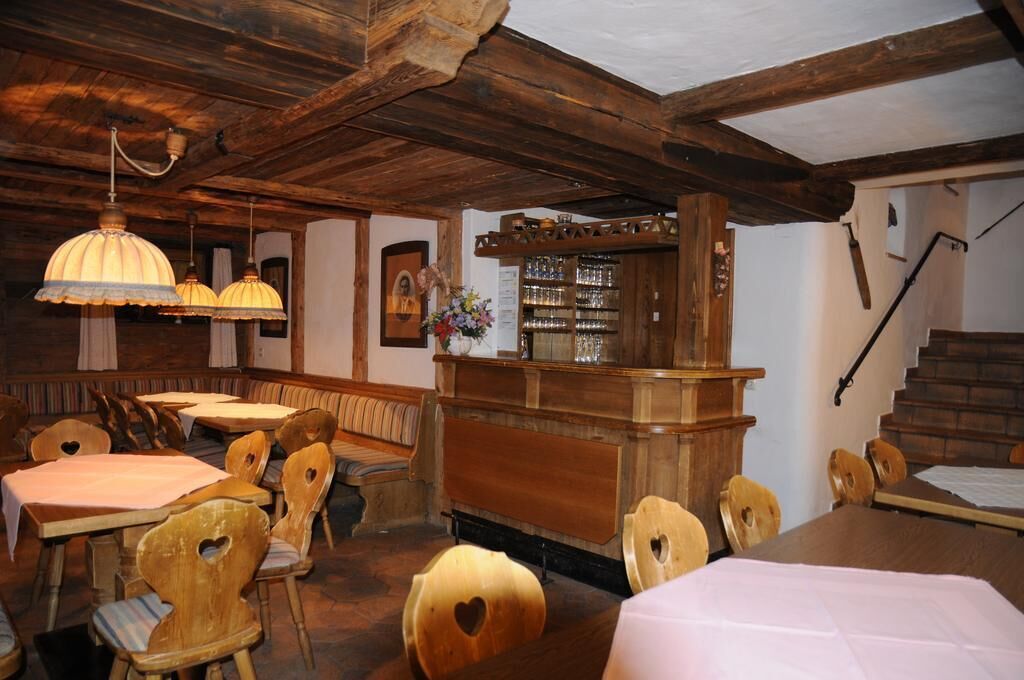 Uma área de jantar rústica com mesas e cadeiras de madeira, um balcão de bar e luminárias pendentes.