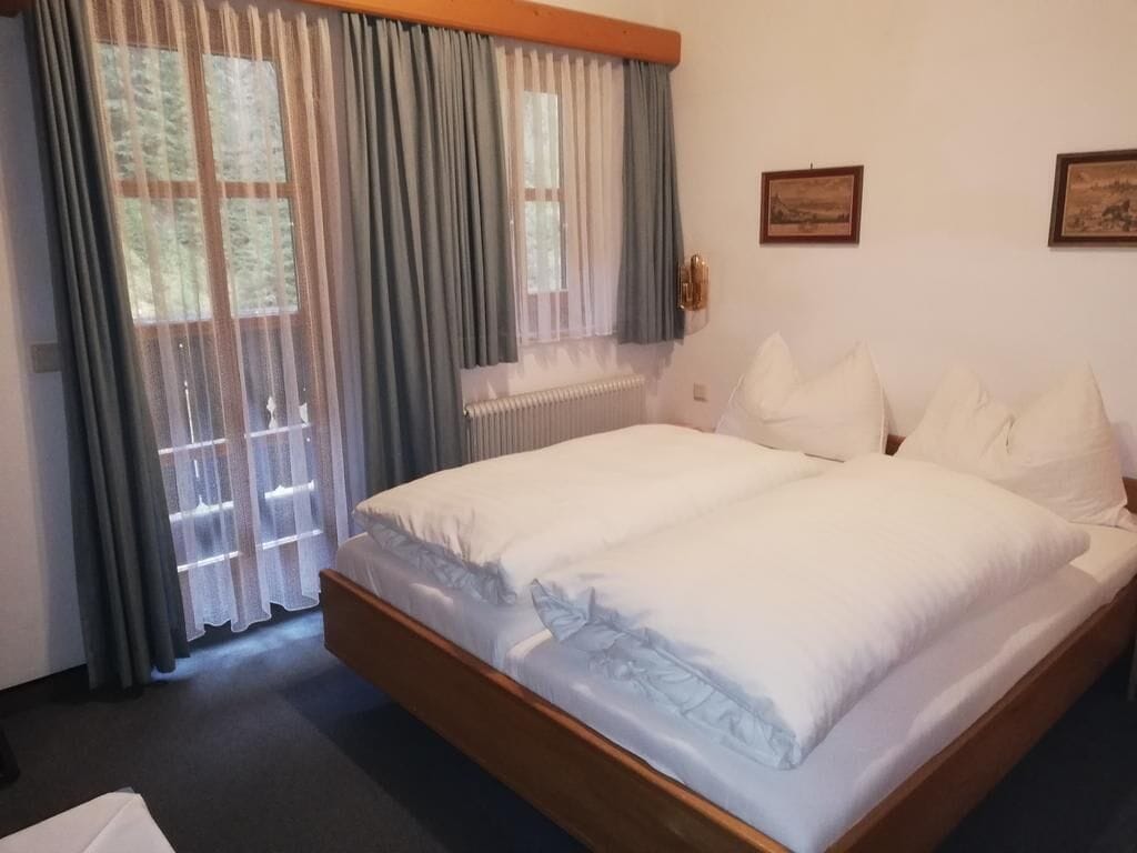 A hotel room with a large bed, a radiator, and two framed pictures on the wall.