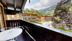 Een balkon met een tafel en stoelen, met uitzicht op een gebouw met meerdere balkons en een bergachtig landschap.