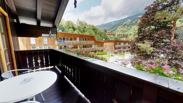 A balcony with a table and chairs, overlooking a building with multiple balconies and a mountainous landscape. - Pension Lederergütl (Saalbach-Hinterglemm)