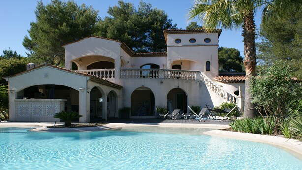 Eine Villa im mediterranen Stil mit Swimmingpool, Rundbogenportalen und einem Balkon mit Blick auf den Pool.