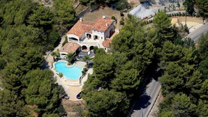 Eine Vogelperspektive zeigt eine Villa mit Swimmingpool, umgeben von dichten Kiefern.