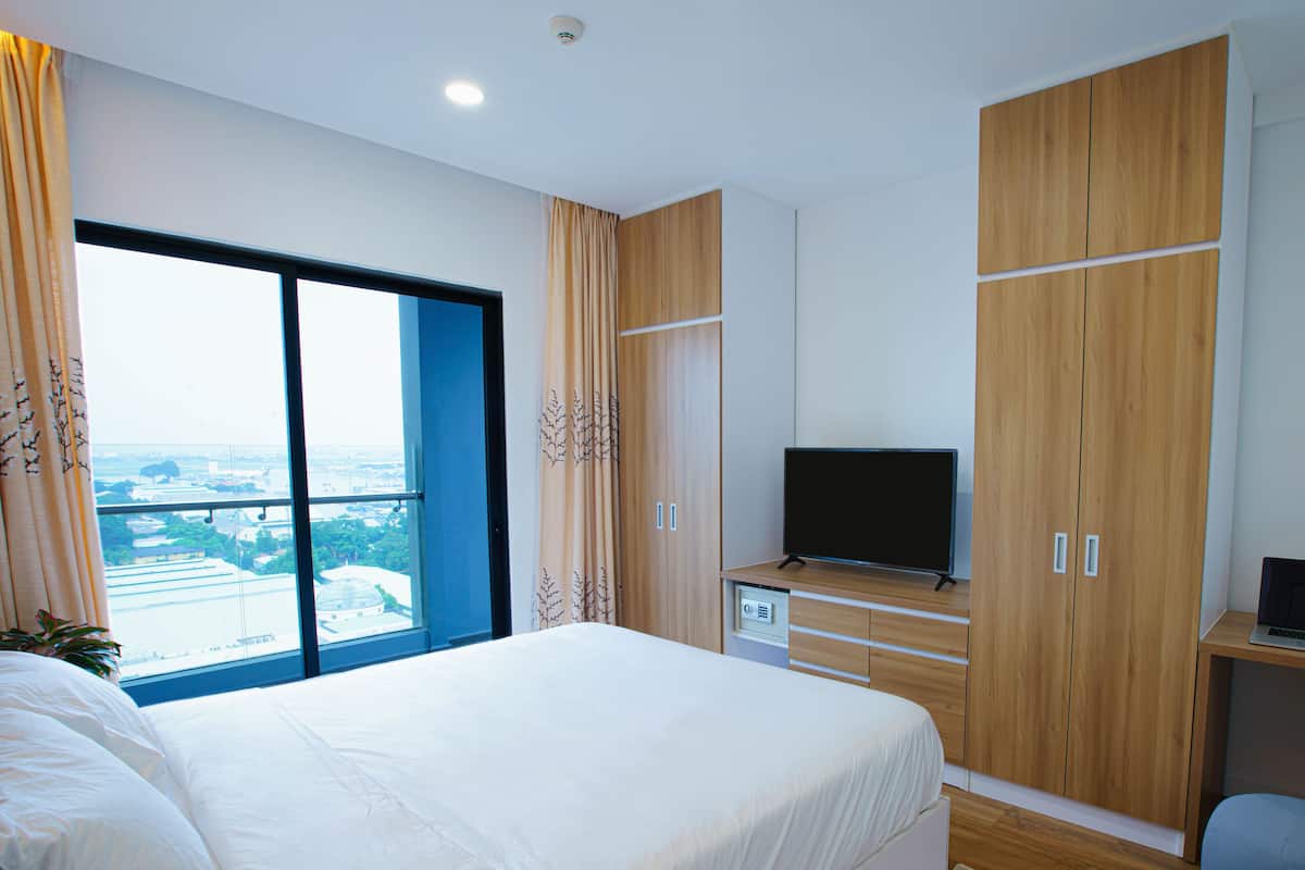 A bedroom with a large bed, a TV, a desk with a laptop, and a wardrobe.