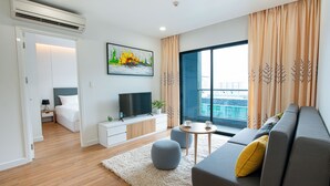 A modern living room with a grey sofa, a flat-screen TV, a small round table with a cup, and a large window with curtains. - Republic Plaza Serviced Apartment (Ho Chi Minh City)