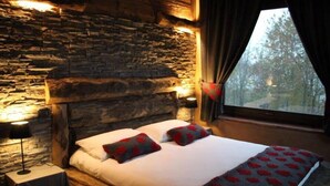 Una cama con cabecera de piedra, dos almohadas y una manta con estampado rojo.