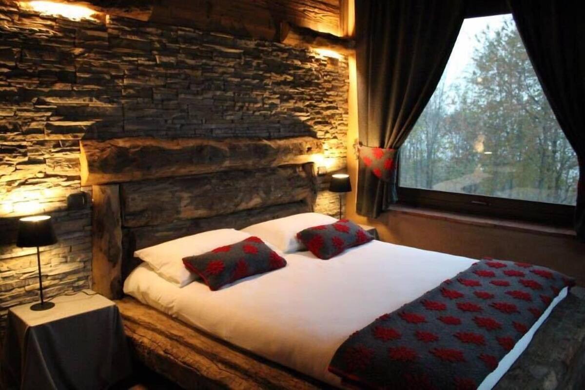 A bed with a stone headboard, two pillows, and a blanket with a red pattern.