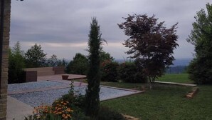 Un jardín con un patio, un árbol alto y vistas del paisaje.