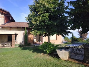 Ein Haus mit Terrasse, Sitzgelegenheiten im Freien und einem großen Baum, der Schatten spendet.