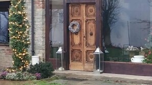 Un edificio rústico con una puerta de madera, un adorno de ramas y un árbol de Navidad iluminado.
