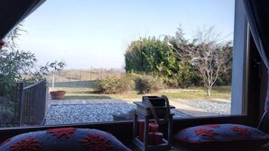 Una habitación con vistas a un jardín, una mesa de madera con velas y dos almohadas con motivos florales rojos.