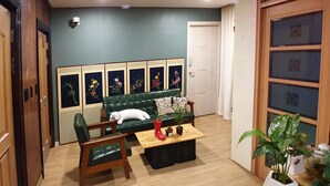 A room with a green sofa, two wooden chairs, a small table with a red pot, and a potted plant. - U Guesthouse 2 in Yeonnam Caters to Women - Hostel (Seoul)