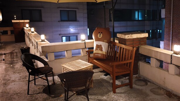 A balcony with a wooden chair, a small table, and a large umbrella providing shade. - U Guesthouse 2 in Yeonnam Caters to Women - Hostel (Seoul)