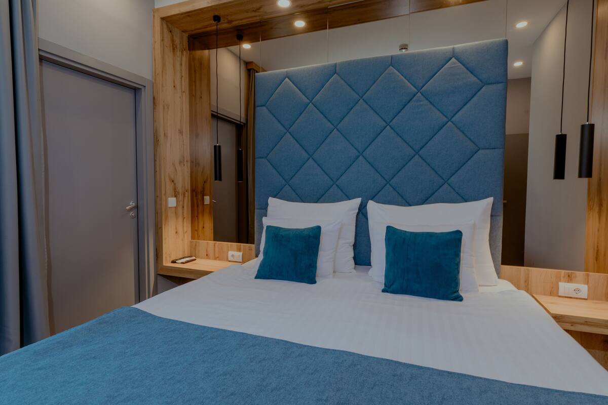 A modern bedroom with a large bed, wooden headboard, and a nightstand with a phone.