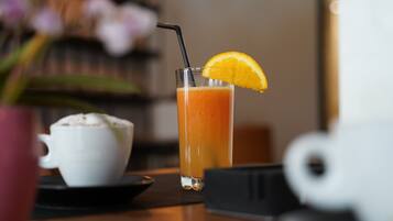 A glass of orange juice with a straw and a slice of orange on the rim, a white cup, and a small black object on a table.