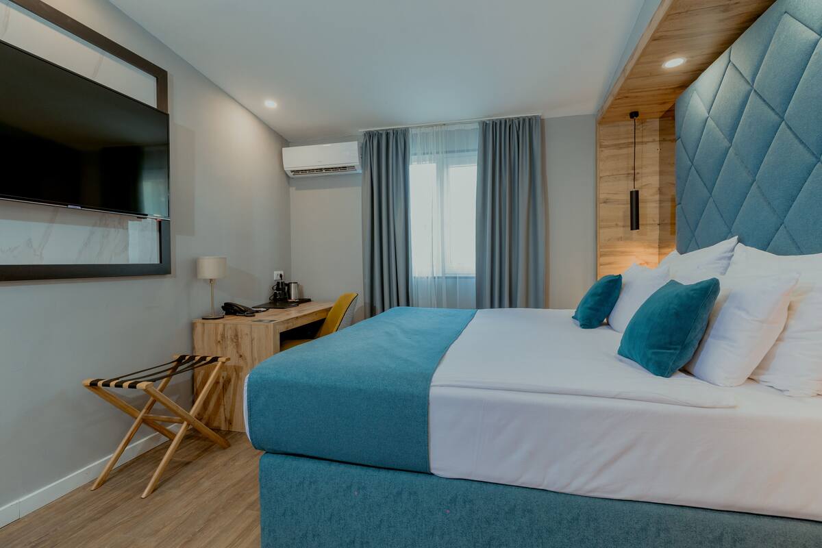 A modern hotel room with a large bed, a desk, and a TV mounted on the wall.