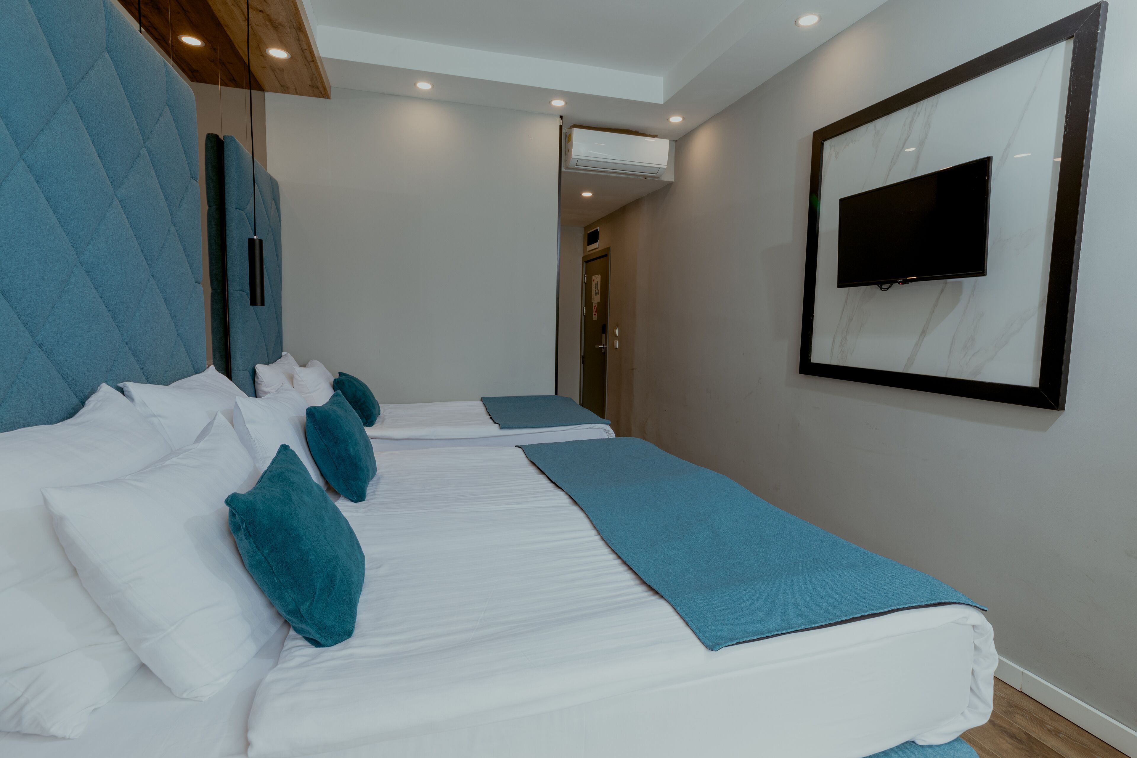Habitación de hotel con dos camas, un televisor montado en la pared e iluminación empotrada en el techo.