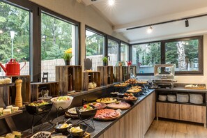 A buffet with various food items and a view of the outdoors through large windows. - Nobel Gallery Hotel (Belgrade)