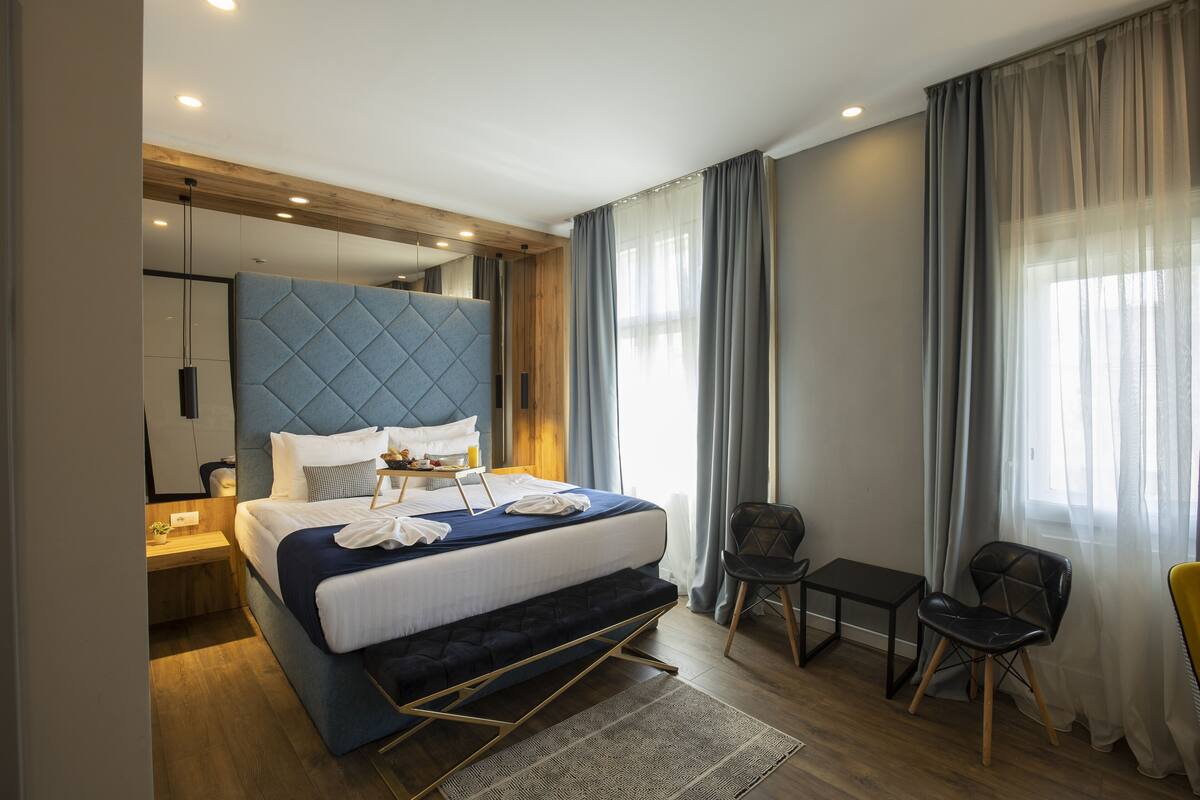 A modern hotel room with a large bed, a desk, a chair, and a view of the outdoors.