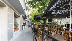 An outdoor cafe with wooden tables and chairs, black umbrellas, and potted plants. - Nobel Gallery Hotel (Belgrade)