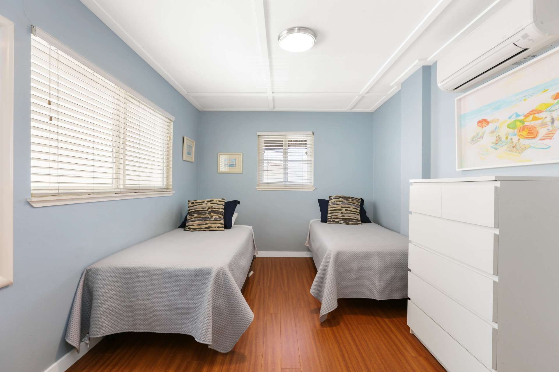 A bedroom with two single beds, a white dresser, and an air conditioning unit.
