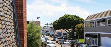 Vista de la calle con coches aparcados, edificios y un árbol grande.