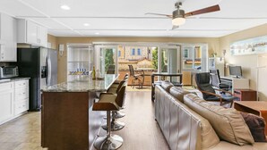 A modern kitchen with a central island, bar stools, a leather sofa, and a dining area with a view of the outside. - Air conditioned Balboa Island Flat, Steps to Balboa Island Ferry, w/Parking. Amazing Location! (Newport Beach)