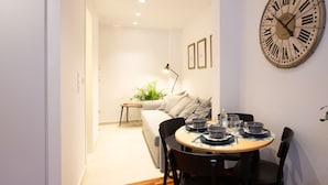A modern dining area with a round table set for two, a large wall clock, and a sofa in the background. - Phaedrus Living: City Luxury Flat Mavromichali (Athens)