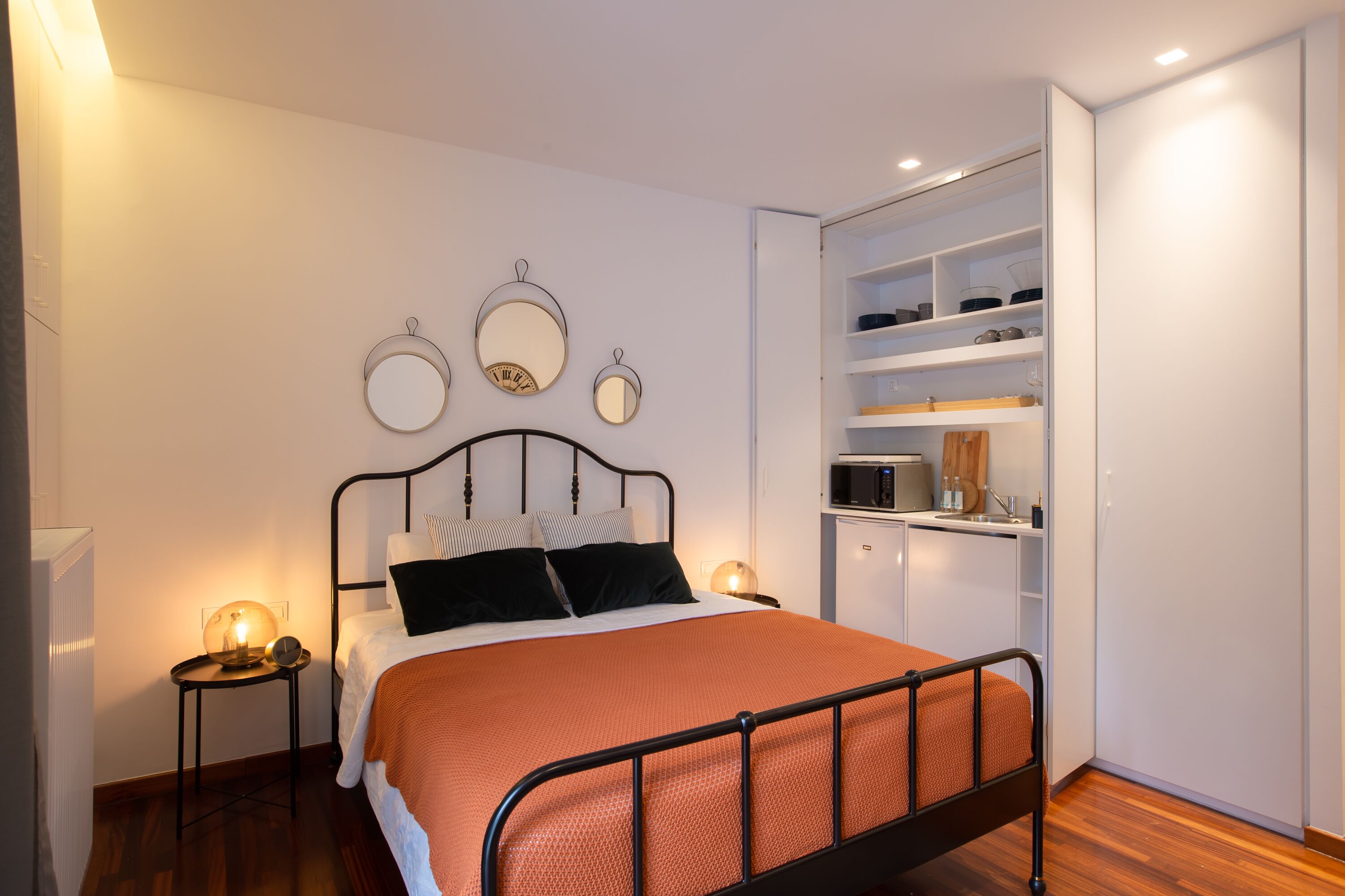 A bedroom with a bed, bedside tables, a wardrobe, and a built-in kitchen area.