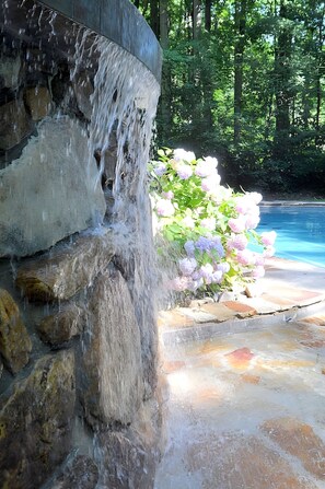 A stone waterfall leading to a pool surrounded by lush greenery. - Almost Heaven - Cozy and Wonderful (Berkeley Springs)