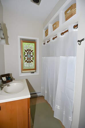 A bathroom with a white sink, wooden cabinets, a decorative window, and a shower curtain.