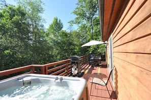 Una terraza de madera con un jacuzzi, mobiliario exterior y una parrilla.