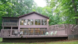A two-story cabin with a balcony and a deck, surrounded by trees. - Dogwood Knoll - Wooded Escape (Berkeley Springs)