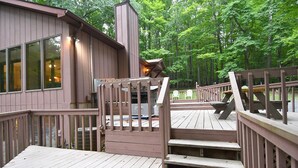A wooden deck with a staircase leading to a covered area, surrounded by trees. - Dogwood Knoll - Wooded Escape (Berkeley Springs)