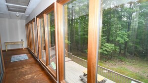 A room with large windows, a wooden floor, a small table, and a bench outside. - Dogwood Knoll - Wooded Escape (Berkeley Springs)