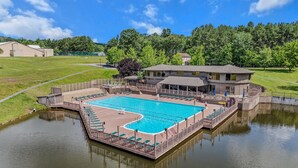 A swimming pool with a wooden deck, surrounded by a fence and a building with a covered area. - Country Comfort -country Escape! (Hedgesville)