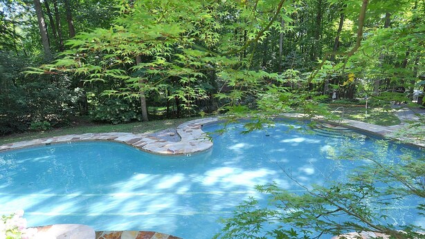 Une piscine entourée d’une terrasse en pierre et d’une végétation luxuriante.