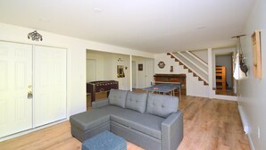 A living room with a grey sectional sofa, a ping pong table, and a staircase leading to another level.